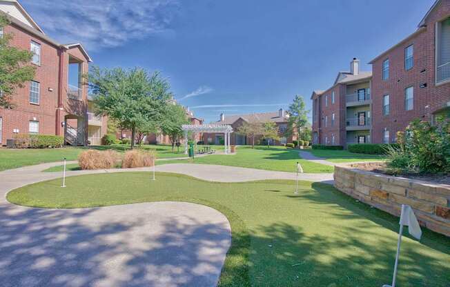 A sunny day at a residential complex with a green lawn and brick buildings.