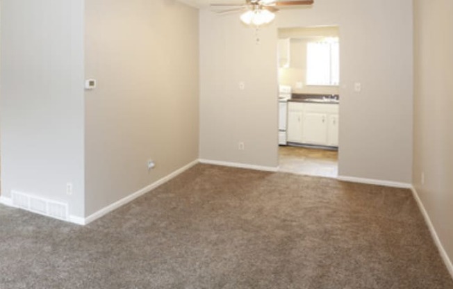 an empty living room with carpet and a kitchen in the background