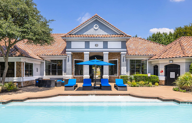 A pool area with a building and blue loungers.