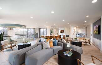 A modern living room with grey couches and wooden chairs.