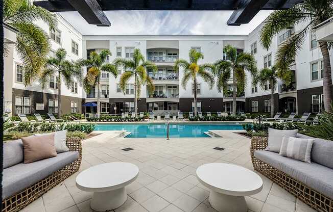 A pool surrounded by palm trees and white furniture.