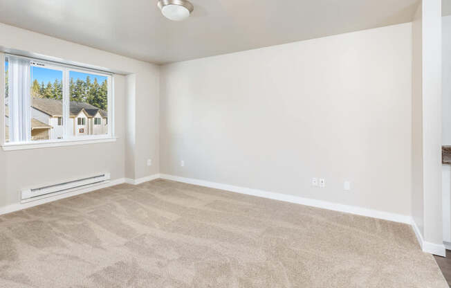 A room with a carpeted floor and a window showing a view of houses.