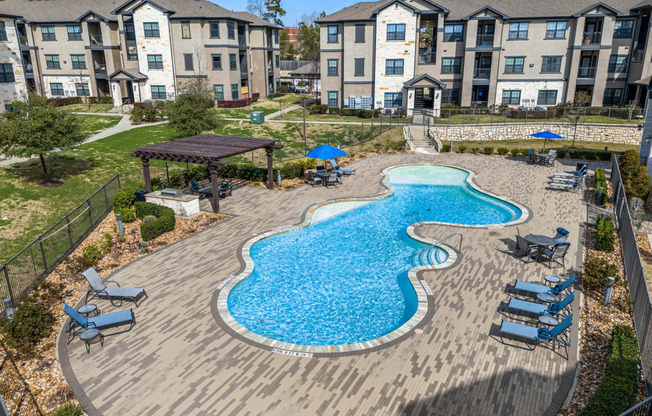 an aerial view of an outdoor pool with lounge chairs and umbrellas in front