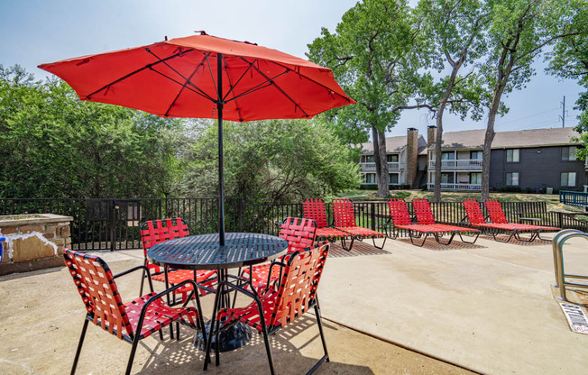 a patio with tables and chairs and a red umbrella
