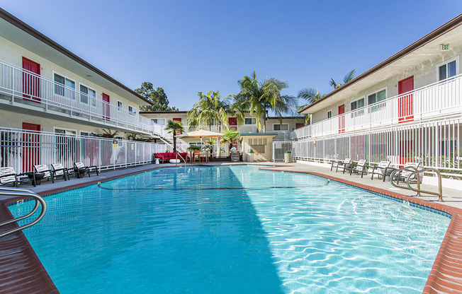 Outdoor swimming pool with sun chairs, a lounge area lined with apartments, and palm trees at Pacific Sands, San Diego, CA