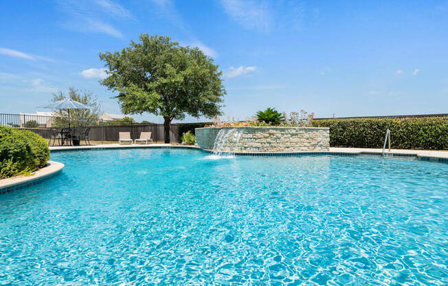 A pool with a waterfall and a tree in the background.