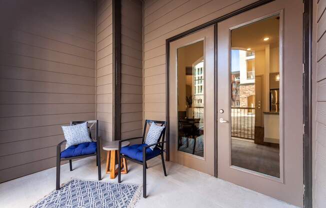 Two chairs and a table are on a porch.