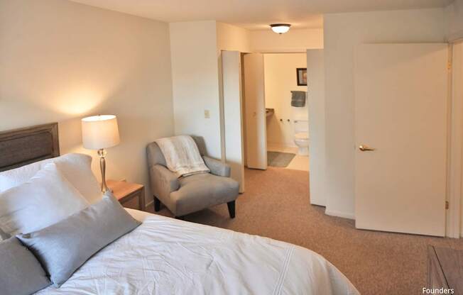 A bedroom with a bed, chair, and bathroom visible through the door.