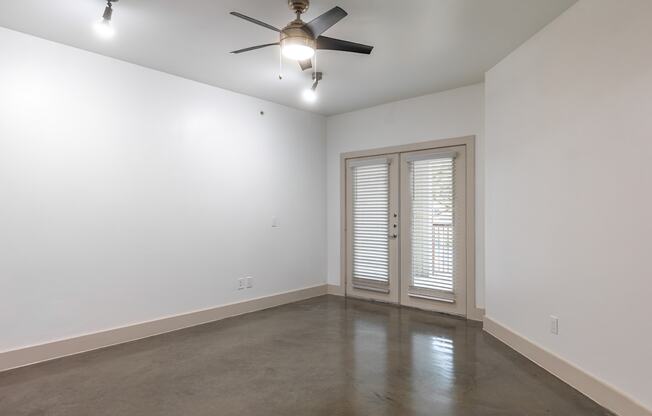 A room with a ceiling fan and sliding glass doors.