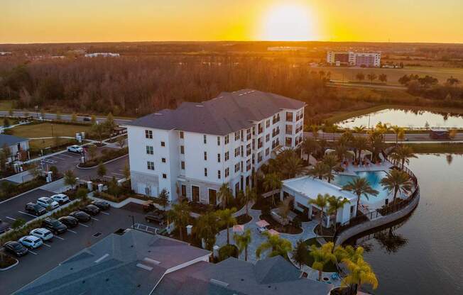 A large white hotel with a pool and a sunset in the background.