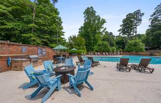 A poolside area with blue chairs and a fire pit.