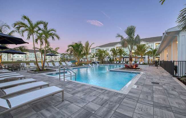 A pool surrounded by palm trees and lounge chairs.