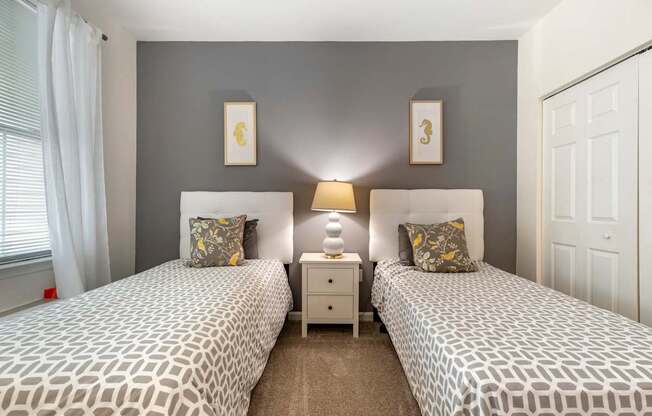 two twin beds in a bedroom with grey walls and a window at Pier Village Apartments, Long Branch, 07740