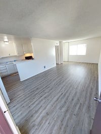 an empty living room with a kitchen in the background