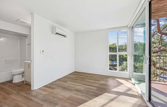 A room with a toilet and a window overlooking a tree.