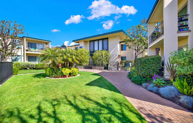 a yard with grass and palm trees in front of an apartment building at Casa Del Amo Apartments, Torrance California