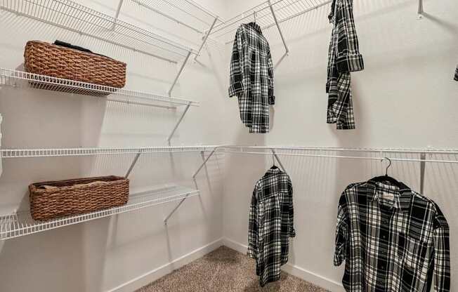 A closet with three shelves and two hanging shirts.