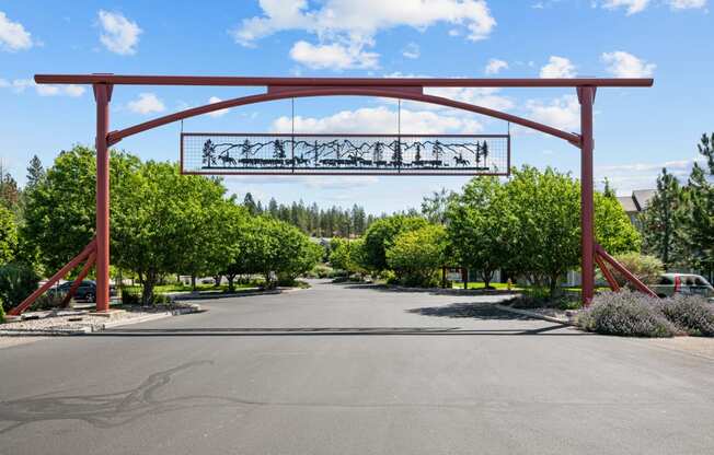 the arch at the end of a road with trees and a driveway