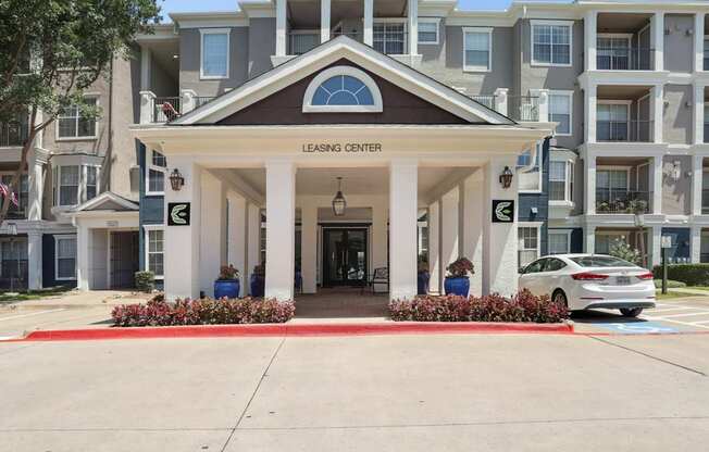 The entrance to the leasing office with white pillars and landscaping at Encore at Buckingham Apartments in Richardson, TX