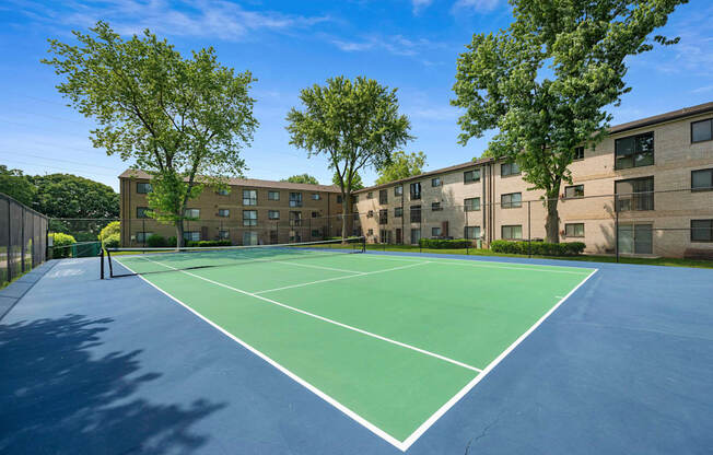 A tennis court is surrounded by apartment buildings.