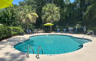 A swimming pool surrounded by trees and chairs.