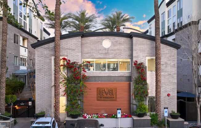 A modern building with a brown facade and a sign that reads "Level" is surrounded by palm trees and other greenery.