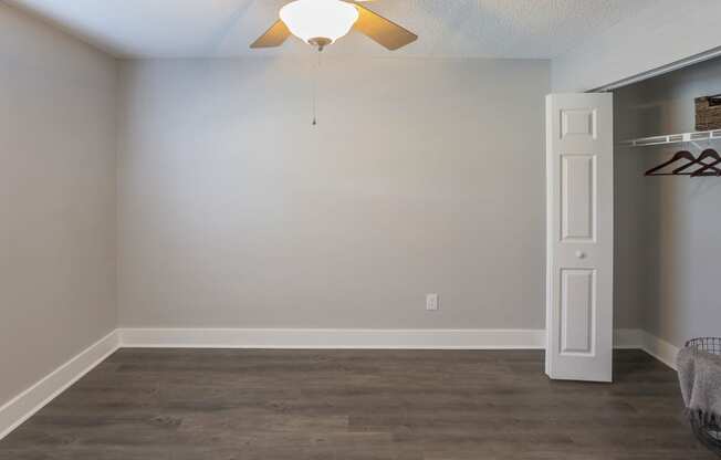 an empty living room with a ceiling fan and a closet