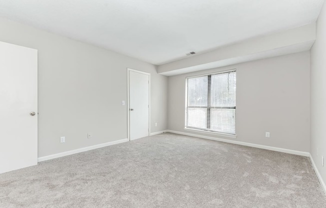 A room with a carpeted floor and a window with blinds.