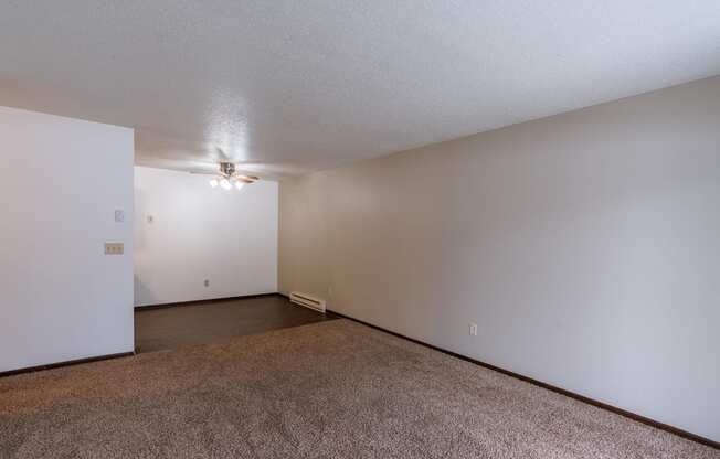 An empty living room with carpet and white walls with a dining room in the background. Fargo, ND Long Island Apartments.