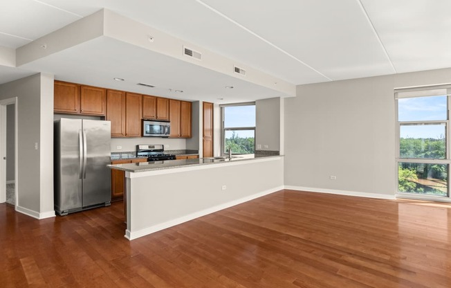 an empty living room with a kitchen and a stainless steel refrigerator