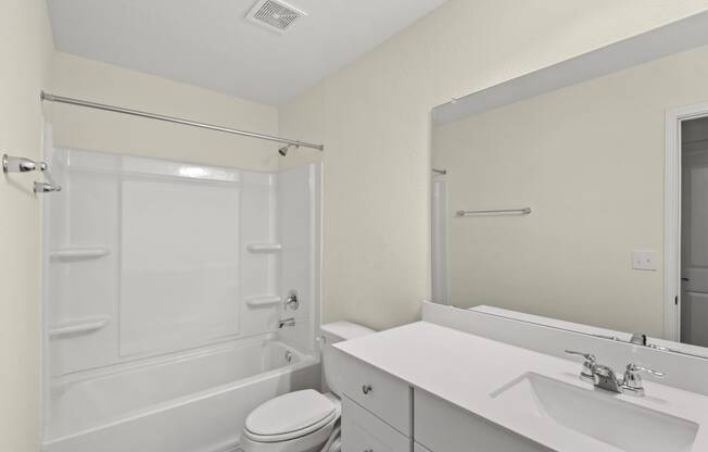 a bathroom with a shower bathtub, big mirror and white cabinets