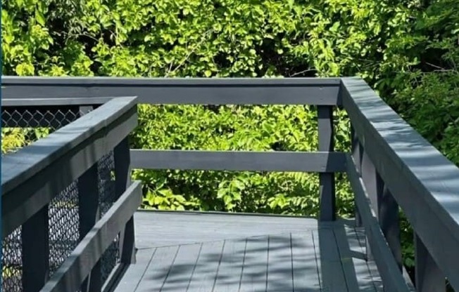 A wooden bridge with a metal railing leads through a lush green forest.