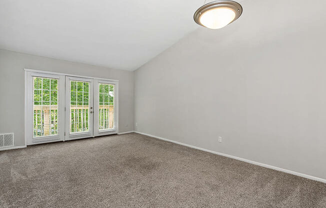 an empty living room with large windows and carpet