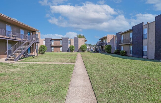 A grassy area in front of apartment buildings with a concrete walkway at The Drake in Bossier City, LA