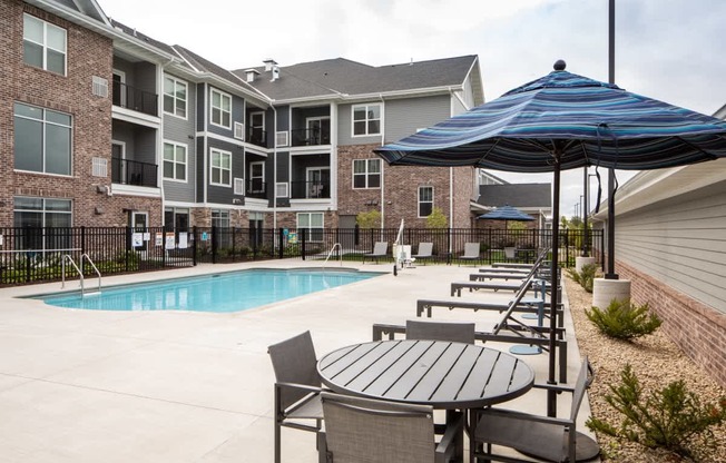 A pool area with a table and chairs and umbrella in front of apartment buildings.