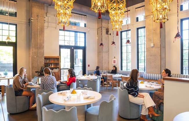 A group of people are sitting at tables in a large room with yellow chandeliers.