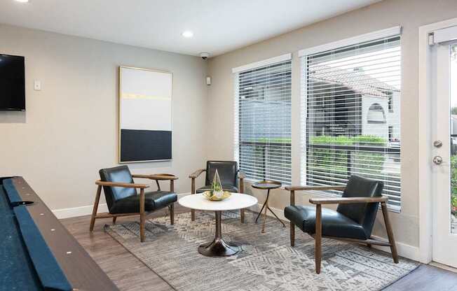 a living room with chairs and a table and large windows