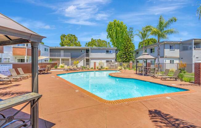 A swimming pool surrounded by a patio with chairs and a building in the background.