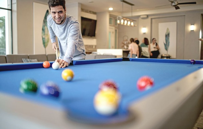 man shooting a pool shot and people behind him hanging out