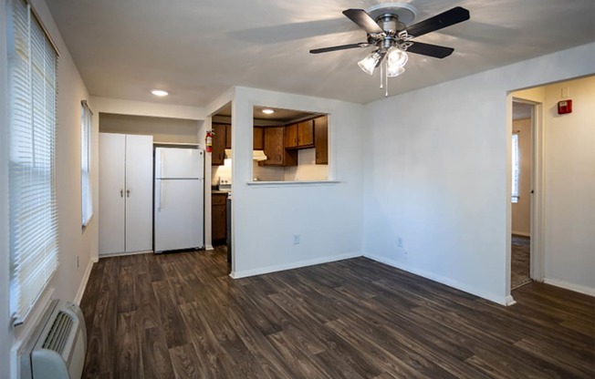 an empty living room with a ceiling fan and a kitchen in the background