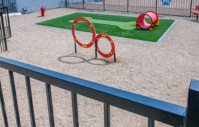 Fifteen 50 apartments Las Vegas Dog park with red park bench, fire hydrant, and dog play tubes and hoops. Features a large patch of artificial grass.