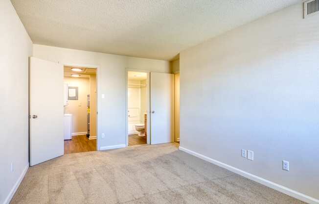 the living room and bedroom of an apartment with carpeting and white walls