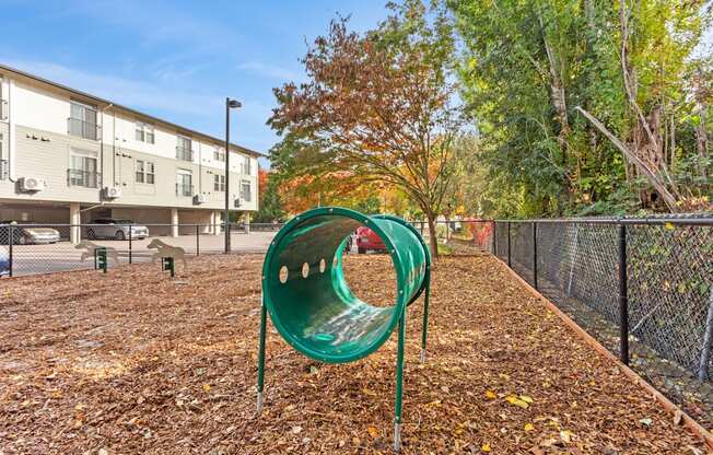 A green playground slide in the middle of a playground surrounded by a fence.