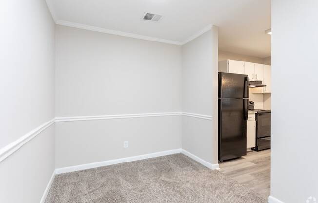 an empty room with white walls and a kitchen with a black refrigerator