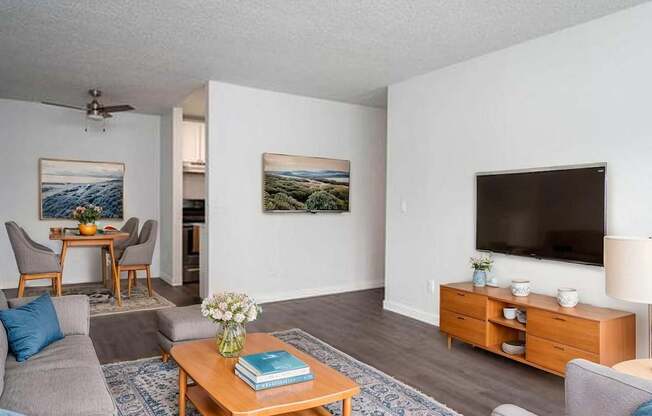 A living room with a grey couch, a wooden coffee table, a flat screen TV, and a painting on the wall.