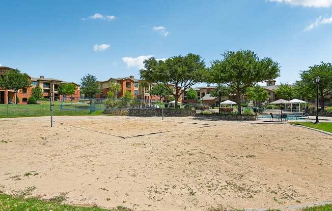 A sandy area in front of a building with trees and umbrellas.