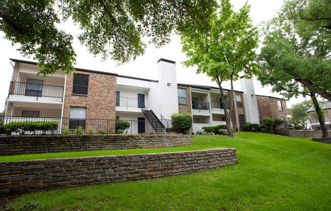 exterior view of apartments with a green lawn and stone retaining wall