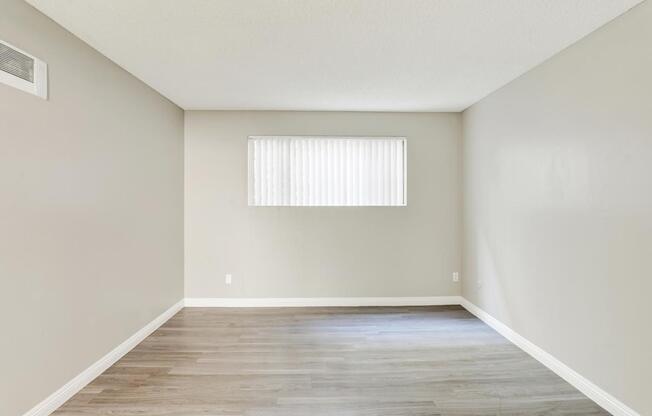 A room with wooden flooring and a window with blinds.