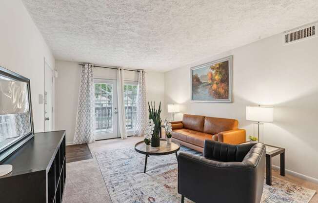 A living room with a brown leather couch, a black armchair, a coffee table, and a painting on the wall.