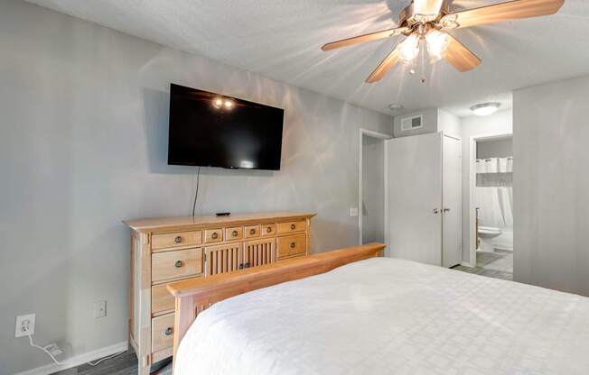 A bedroom with a bed, dresser, and a flat screen TV mounted on the wall.